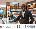 Smiling professional hotel concierge standing confidently at reception desk 114434409