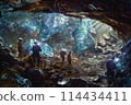Miners with hardhats exploring expansive underground cave illuminated by artificial light 114434411