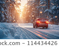 Car driving on a snow-covered road in the forest against the setting sun. 114434426