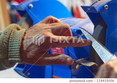 Sharpening a knife on a blue machine in the workshop Sharpening a knife on a blue machine in the workshop 114435056