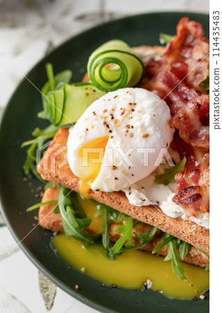 Toasts sandwich with poached egg, cucumber, arugula, bacon and cream cheese on printed tile background for healthy breakfast, close up Toasts sandwich with poached egg, cucumber, arugula, bacon and cream cheese on printed tile background for healthy breakfast, close up 114435483
