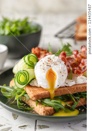 Toasts sandwich with poached egg, cucumber, arugula, bacon and cream cheese on printed tile kitchen background for healthy breakfast, close up 114435487