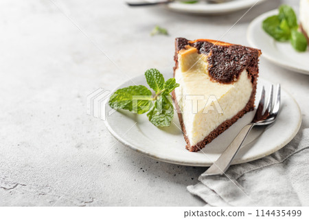 Piece of homemade chocolate cheesecake with mint leave on a plate on white textured background with copy space 114435499