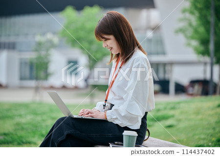 A young woman operating a computer at the park 114437402