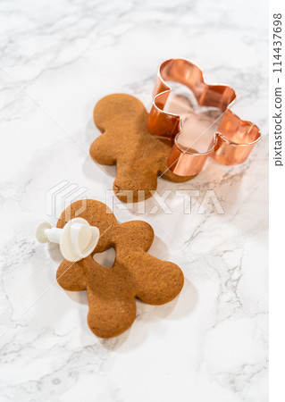 Gingerbread cookies, including a gingerbread man with a heart-shaped cutout, rest on a rustic metal tray against a marble countertop. Gingerbread cookies, including a gingerbread man with a heart-shaped cutout, rest on a rustic metal tray against a marble countertop. 114437698