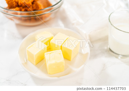 In a cozy kitchen, ingredients are meticulously measured in glass mixing bowls on the kitchen counter, all set to create a delightful homemade pumpkin bundt cake from cake mix. 114437703