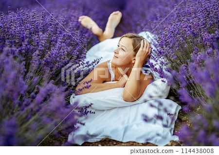 A middle-aged woman lies in a lavender field and enjoys aromatherapy. Aromatherapy concept, lavender oil, photo session in lavender 114438008