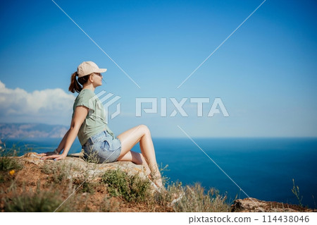 A woman is sitting on a rock overlooking the ocean 114438046