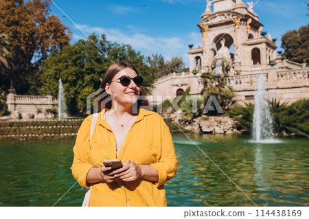 Young female tourist with phone visiting Ciutadella Park in Barcelona. Concept of travel, tourism and vacation in city. Use technology concept, Traveling Europe 114438169