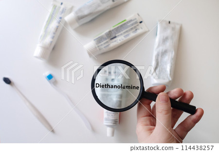 Dangerous toothpaste ingredient diethanolamine. Checking the composition of toothpaste with a magnifying glass against the background of many tubes 114438257
