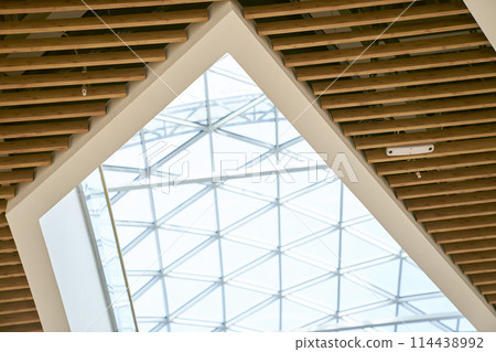 The ceiling is made of wooden elements and transparent glass. Skylight glass roof, with space for copying. Natural lighting of an eco-building to save energy costs. High quality photo The ceiling is made of wooden elements and transparent glass. Skylight glass roof, with space for copying. Natural lighting of an eco-building to save energy costs. High quality photo 114438992