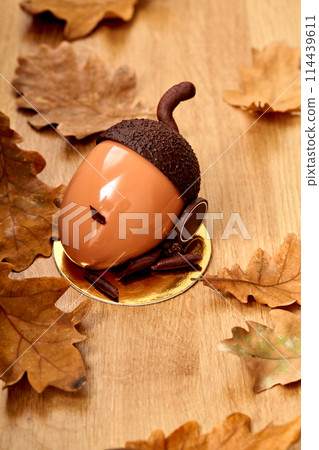 Chocolate acorn shaped cake on wooden surface among oak leaves Chocolate acorn shaped cake on wooden surface among oak leaves 114439611