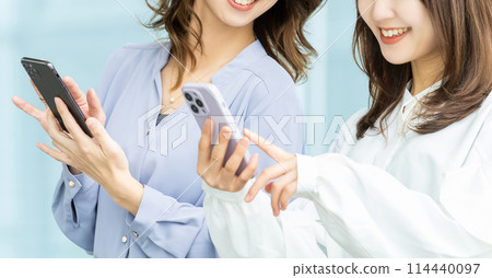 兩位女商人看著智慧型手機並交談 兩位女商人看著智慧型手機並交談 114440097