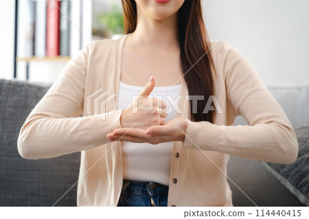 A young deaf woman is sitting on a couch and making a sign Language to communicate. 114440415