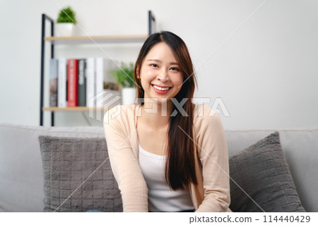 A portrait of beautiful young asian woman with long brown hair is sitting on a couch and smiling A portrait of beautiful young asian woman with long brown hair is sitting on a couch and smiling 114440429