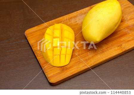 Mango. Close up of fresh ripe mango fruit with leaves over dark wooden table background with green leaves Mango. Close up of fresh ripe mango fruit with leaves over dark wooden table background with green leaves 114440853