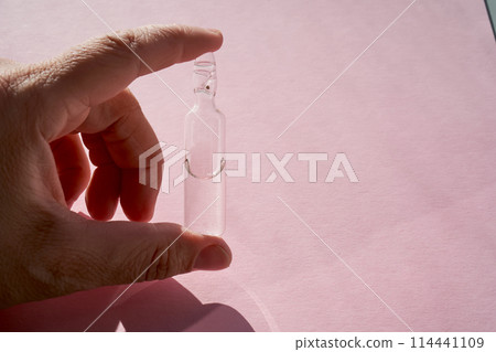 Ampoule for injection with medicines on a pink background in hand. 114441109