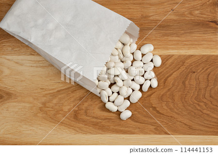 heap of white beans in paper bag on wooden background, top view 114441153