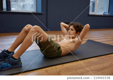Concentrated fitness boy doing abs exercise lying on mat 114441536
