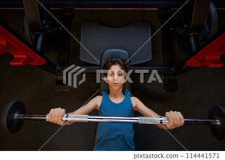 Preteen boy doing bench press training with barbell at gym 114441571