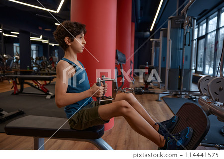 Active preteen boy child training at exercise machines in modern gym 114441575