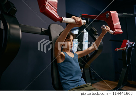 Active athletic preteen boy training arms muscles at gym 114441603