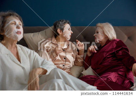 Happy senior female friends with cotton mask on face having nice conversation 114441634