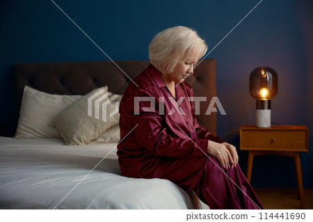 Elderly woman wearing pajamas sitting on bed feeling loneliness Elderly woman wearing pajamas sitting on bed feeling loneliness 114441690