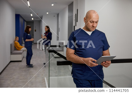 Mature adult man doctor in uniform with digital tablet in clinic corridor 114441705