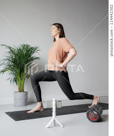 young Caucasian woman does sports online, stretches, practices yoga, meditation in gym 114442302
