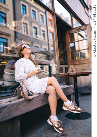 Tourist woman enjoys architecture of city streets with cup of coffee. Travel and vacation concept. Tourist woman enjoys architecture of city streets with cup of coffee. Travel and vacation concept. 114443135
