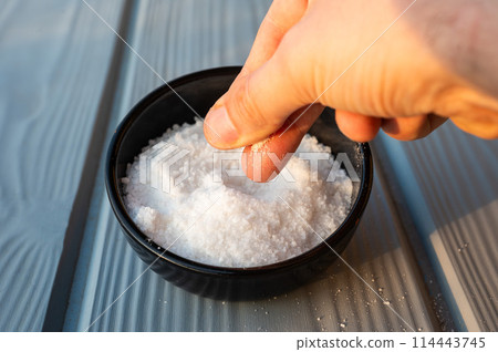 Cook's hand taking coarsed sea salt out of a black bowl, Belgium Cook's hand taking coarsed sea salt out of a black bowl, Belgium 114443745
