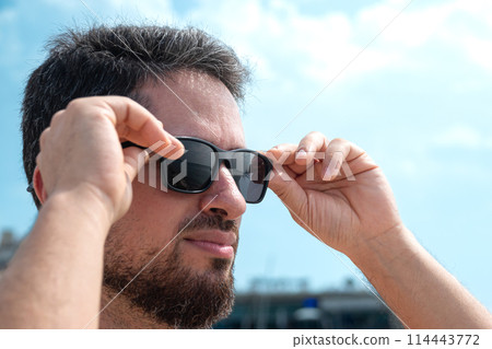 Young adult man taking off his sunglasses contemplating beautiful beach horizon Young adult man taking off his sunglasses contemplating beautiful beach horizon 114443772