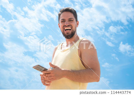 Young adult Laughing on beach with cell phone looking camera and sunny blue sky Young adult Laughing on beach with cell phone looking camera and sunny blue sky 114443774
