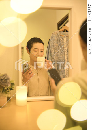 A middle-aged woman relaxing and reading a book while drinking coffee and looking at her smartphone A middle-aged woman relaxing and reading a book while drinking coffee and looking at her smartphone 114445227