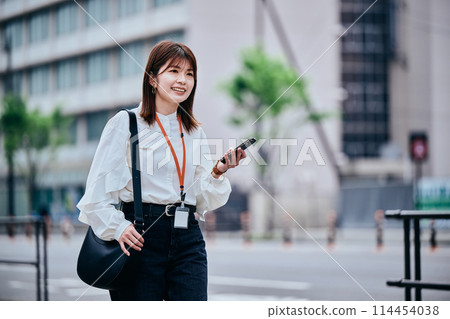 A young woman walking while operating a smartphone 114454038