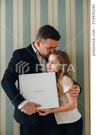 A dad and daughter hold a photo book in a white leather cover  A dad and daughter hold a photo book in a white leather cover  114456280