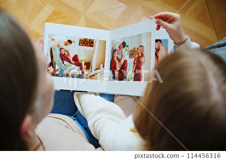 mother and daughter flips through a book with photos of dad and pregnant mom. mother and daughter flips through a book with photos of dad and pregnant mom. 114456316