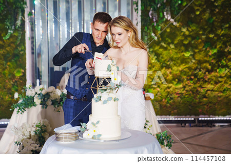 The bride and groom cut the wedding cake at the banquet.  114457108