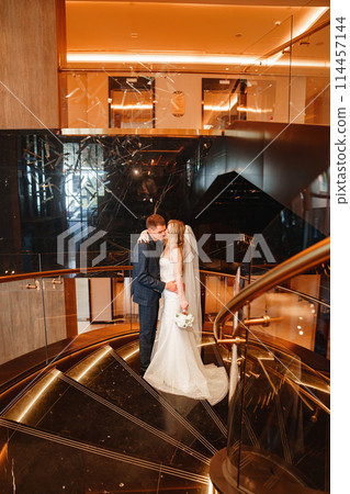 Bride and groom embracing on a golden spiral staircase.  114457144