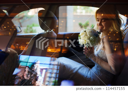 a beautiful and happy bride with a bouquet in a car through the glass. 114457155