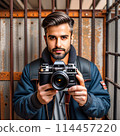 A dark-skinned male photographer with a beard in prison.  114457220