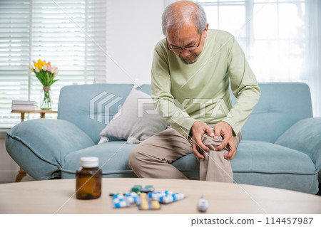 Old age. Asian senior man retirement knee joint pain on sofa, Elderly old man sitting down hands hold knee, Grandfather people health care bone problem at home 114457987