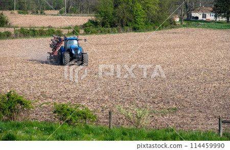 Blue farm tractor pulls disc harrow cultivator over agricultural field Blue farm tractor pulls disc harrow cultivator over agricultural field 114459990