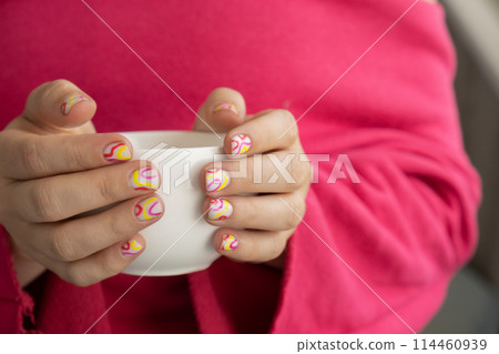 Pastel softness colorful manicured nails. Woman holding white cup of coffee or tea showing her new summer manicure in colors of pastel palette. Simplicity decor fresh spring vibes earth-colored 114460939