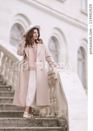 woman in elegant coat and hat against an intricate architectural backdrop, harmoniously blending modern fashion with historical allure. The soft daylight adds to its timeless appeal. woman in elegant coat and hat against an intricate architectural backdrop, harmoniously blending modern fashion with historical allure. The soft daylight adds to its timeless appeal. 114462629