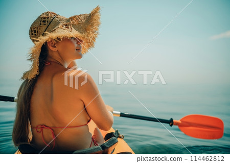 Woman in kayak back view. Happy woman with long hair in a swimsuit and hat floating in kayak on the sea. Summer holiday vacation. Summer holidays vacation at sea. 114462812