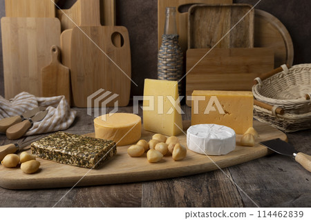 Cheese assorted on a wooden board, rustic style. Several varieties of whole cheese: parmesan, tilsiter, halloumi with spices, camembert, smoked bocconcini, cheddar. Cheese plate. 114462839
