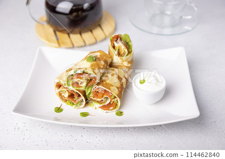 Pancakes with salmon (trout), sour cream, greenstuff and tea. Thin, not sweet blinchiki stuffed with red fish. Traditional Russian and Ukrainian dish. Feast of Maslenitsa. Selective focus, close-up. 114462840
