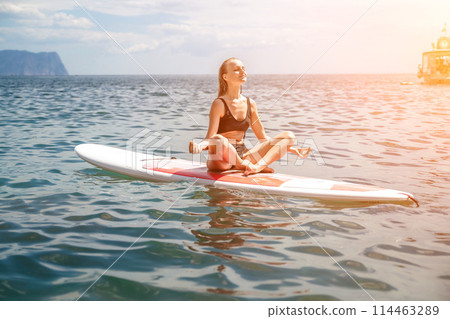 Woman sup sea. Sports girl on a surfboard in the sea on a sunny summer day. In a black bathing suit, he sits on a sapa in the sea. Rest on the sea. 114463289